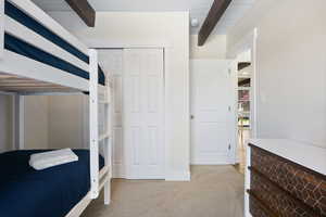 Bedroom featuring light carpet, a closet, and beamed ceiling