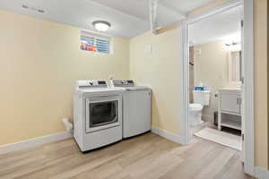 Washroom featuring washer and clothes dryer, light wood finished floors, a textured ceiling, and baseboards