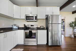 Kitchen featuring stainless steel appliances, white cabinets, beamed ceiling, and dark wood finished floors