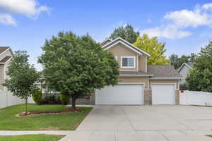 View of property hidden behind natural elements featuring driveway, stucco siding, an attached garage, a shingled roof, and brick siding