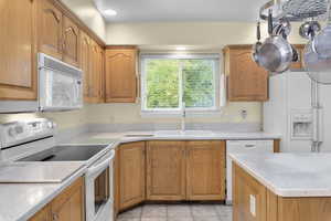 Kitchen with white appliances, a sink, light countertops, light tile patterned flooring, and brown cabinetry