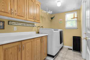 Washroom with cabinet space, washer and clothes dryer, light tile patterned floors, and baseboards