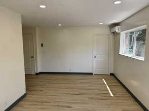 Empty room featuring a wall mounted AC, baseboards, recessed lighting, and light wood finished floors