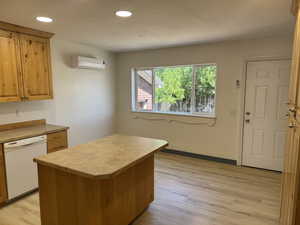 Kitchen with dishwasher, a wall mounted air conditioner, light countertops, light wood finished floors, and a kitchen island