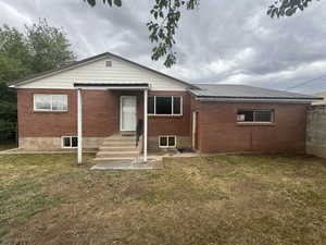 Back of house with a lawn, brick siding, and entry steps