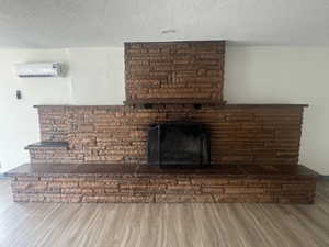 Detailed view of a wall mounted AC, wood finished floors, a textured ceiling, and a fireplace