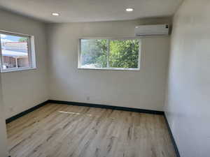Empty room featuring a wall unit AC, wood finished floors, baseboards, and recessed lighting