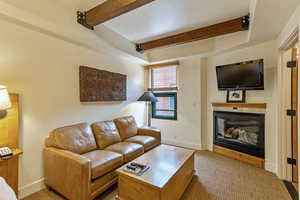 Living room featuring beamed ceiling, carpet flooring, baseboards, and a glass covered fireplace