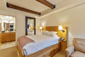 Bedroom featuring beam ceiling, light tile patterned floors, and connected bathroom