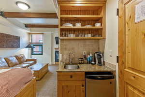 Kitchen featuring dishwashing machine, a sink, backsplash, light colored carpet, and stone countertops