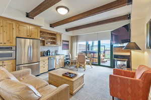 Living area with light carpet, a multi sided fireplace, beam ceiling, and bar area