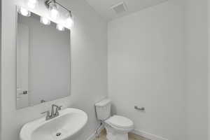Half bath featuring a sink, toilet, baseboards, and wood finished floors