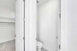 Bathroom featuring baseboards, toilet, and a walk in closet