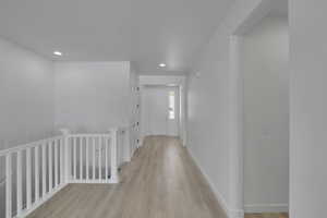 Corridor featuring light wood-style flooring, an upstairs landing, and recessed lighting
