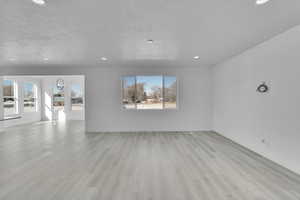 Unfurnished living room featuring a textured ceiling, light wood-type flooring, recessed lighting, and baseboards