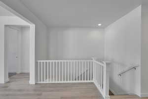 Corridor with an upstairs landing, recessed lighting, wood finished floors, and baseboards