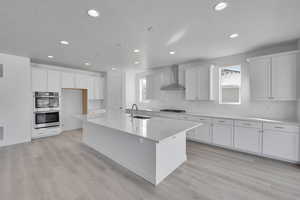 Kitchen with a sink, wall chimney exhaust hood, double oven, backsplash, and recessed lighting