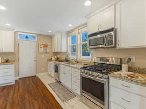 Kitchen with appliances with stainless steel finishes, a sink, white cabinets, recessed lighting, and light stone counters
