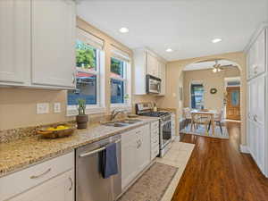 Kitchen featuring stainless steel appliances, a sink, arched walkways, white cabinets, and light stone counters