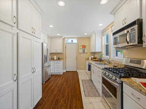 Kitchen with appliances with stainless steel finishes, a sink, white cabinets, baseboards, and recessed lighting