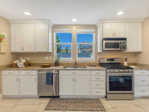 Kitchen featuring stainless steel appliances, a sink, white cabinets, recessed lighting, and light stone countertops