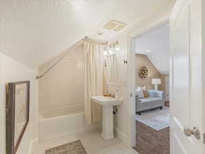Ensuite bathroom with vaulted ceiling, shower / bath combo with shower curtain, a textured ceiling, baseboards, and a sink