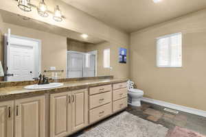Bathroom featuring a stall shower, vanity, baseboards, stone tile flooring, and toilet