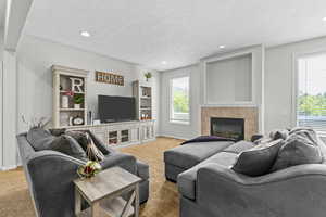 Living room with light carpet, plenty of natural light, a tile fireplace, a textured ceiling, and baseboards