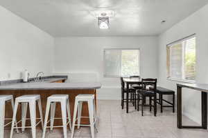 Dining space with a textured ceiling, light tile patterned flooring, and bar with sink