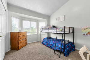Bedroom featuring carpet flooring, vaulted ceiling, a textured ceiling, baseboards, and a closet
