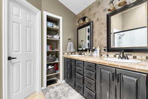 Bathroom with double vanity, lofted ceiling, and a shower