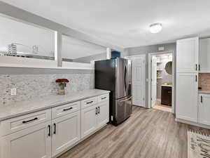 Kitchen featuring stainless steel refrigerator with ice dispenser, decorative backsplash, white cabinetry, and light wood-type flooring