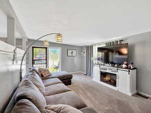 Carpeted living room featuring baseboards, a warm lit fireplace, and a chandelier