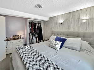 Carpeted bedroom with a textured ceiling, wooden walls, and a closet