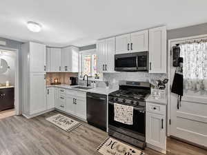 Kitchen with stainless steel appliances, a sink, light countertops, decorative backsplash, and white cabinetry