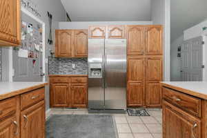 Kitchen featuring stainless steel fridge, light tile patterned floors, light countertops, and tasteful backsplash