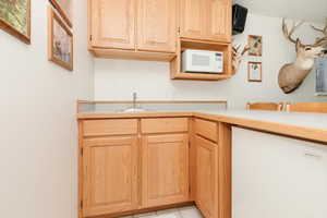 Kitchen featuring white microwave, a sink, light countertops, light brown cabinetry, and light tile patterned floors