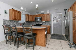 Kitchen featuring appliances with stainless steel finishes, decorative backsplash, a peninsula, lofted ceiling, and brown cabinetry