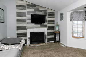 Living room featuring an accent wall, carpet, lofted ceiling, a fireplace, and baseboards