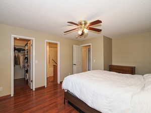 Bedroom featuring wood finished floors, a walk in closet, a closet, a textured ceiling, and ceiling fan
