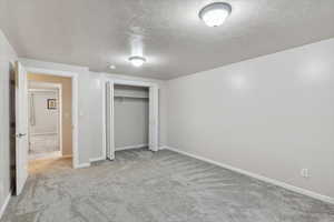Unfurnished bedroom featuring a textured ceiling, carpet, baseboards, and a closet