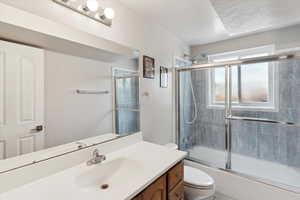 Bathroom with toilet, vanity, and bath / shower combo with glass door