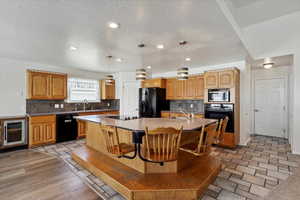 Kitchen with black appliances, an island with sink, a textured ceiling, tasteful backsplash, and a sink