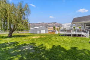 View of grassy yard with a detached garage, an outbuilding, a deck with mountain view, and stairs