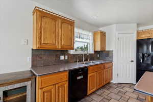 Kitchen with black appliances, a sink, wine cooler, decorative backsplash, and stone finish floors