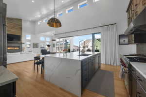 Kitchen with under cabinet range hood, appliances with stainless steel finishes, a towering ceiling, open floor plan, and a sink