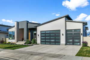 Contemporary house with concrete driveway, a garage, stucco siding, and a front yard