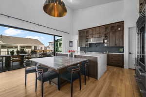 Kitchen featuring a towering ceiling, under cabinet range hood, dark brown cabinetry, light wood-style floors, and an island with sink
