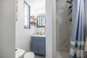 Bathroom with a marble finish shower, vanity, toilet, and lofted ceiling