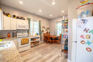 Kitchen featuring white appliances, light wood-style floors, recessed lighting, healthy amount of natural light, and white cabinetry